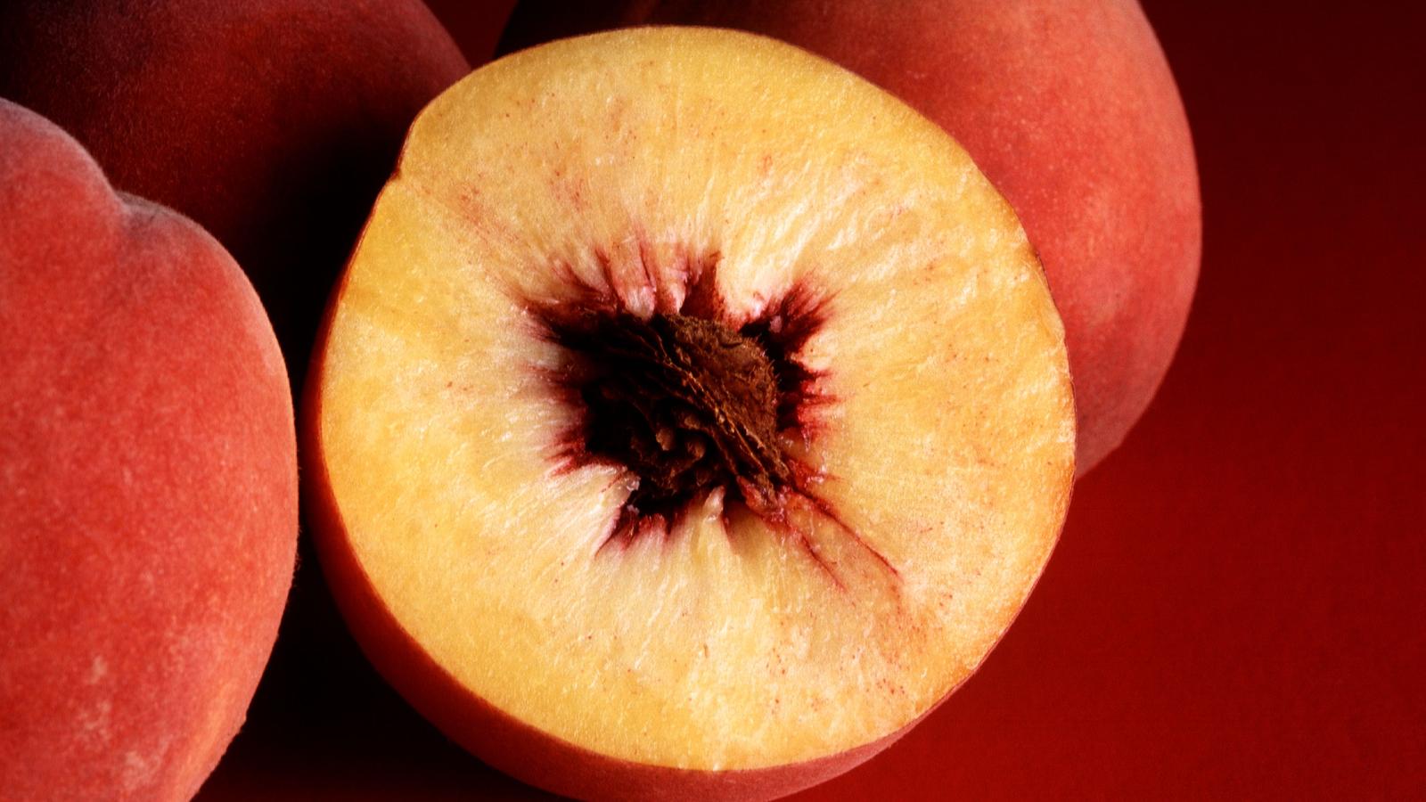 Whole peach beside two halved peaches showing the pit
